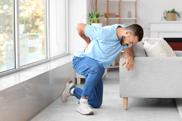 Young man suffering from back pain near sofa at home