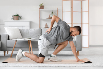 Sporty young man suffering from back pain on fitness mat at home