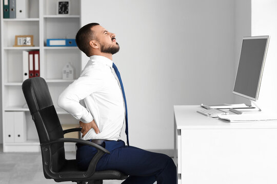 Young businessman suffering from back pain at table in office