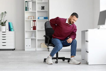 Young man suffering from back pain at table in office