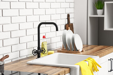 Rack with clean plates on wooden table near sink in kitchen