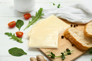 Board with slices of delicious processed cheese with fresh vegetables and bread on white wooden...