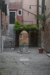 Un piccolo campiello di Venezia con una vera da pozzo, un arco che affaccia su un canale, una scala...