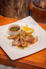 High angle shot of grilled pork neck with a cup of spicy sauce on dish and garnished with a piece of lemon and place on wooden serving board