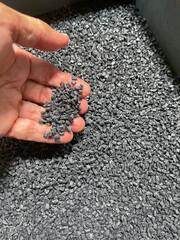 plastic raw material, hand holding a handful of black plastic pellets on a gray plastic drawer, production of plastic parts, plastic injection, spilling of plastic grains with glass fiber