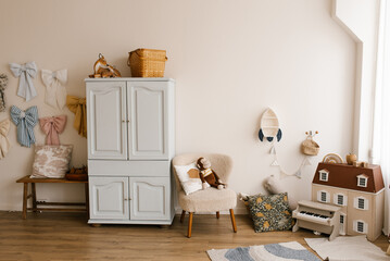 Children room with white wall and colorful bows hanging on the wall. Small toy house is on the...