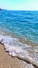 Serene shoreline waves gently lap at the sandy beach under a clear blue sky