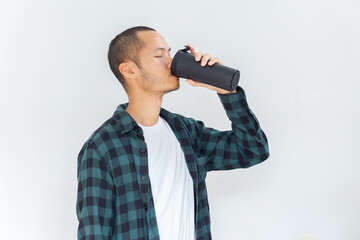 Young asian men wearing flannel and shirt is drinking from black tumbler with smile in isolated white background