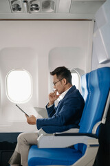 Young Asian executive excels in first class, multitasking with digital tablet, laptop and...