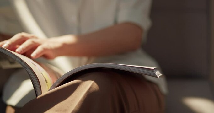 Experience pure bliss as a woman enjoys her well-deserved break, reading her favorite magazine on a comfy sofa, bathed in the gentle warmth of sunlight streaming through the window.
