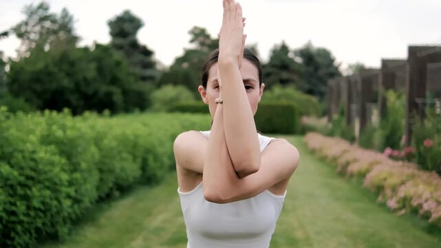Wellness instructor practicing a variation of eagle arms pose in a serene garden environment, promoting relaxation and mindfulness through gentle movement and breath
