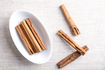 Ceylon cinnamon sticks, cinnamon quills in an oval white bowl on linen. Group of whole dried bark...