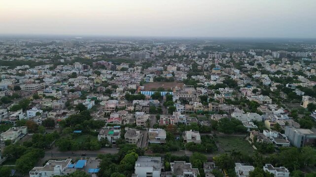 Beautiful aerial above traffic on street through quaint small town in India. Indian city during summer golden hour. Homes along street. Drone view.