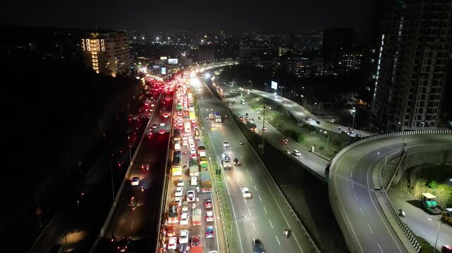 An aerial video shows a service road, fast-moving automobiles, and residential and commercial buildings on an Indian highway that is expanding quickly. The Metro train bridge is currently being built,