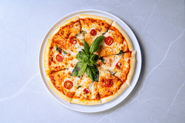 Top View Of Margherita Pizza With Basil Garnish, Top view of a delicious Margherita pizza with fresh basil and cherry tomatoes on a white plate.