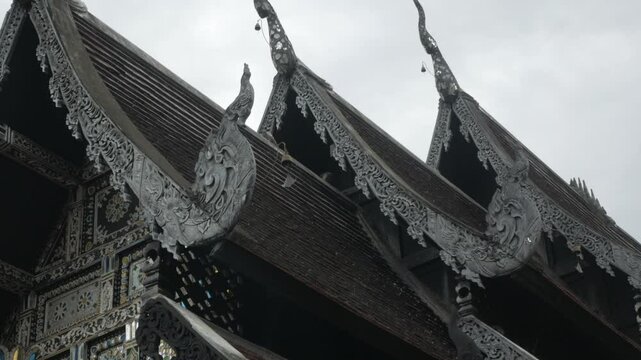 view look to the roof tiles on the temple roof with thai ancient art decoration in buddhist cultural northern style design in daytime with cloudy rainy sky
