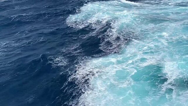 Big wave and white seething foam from a fast sailing cruise ship. Blue turbulent water of the Pacific Ocean. Water of the open ocean on a sunny day. View from a cruise ship.