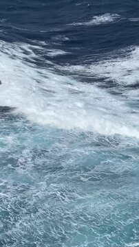 Waves and white seething foam from a cruise ship sailing. Blue turbulent water of the Pacific Ocean. Water of the open ocean on a sunny day. View from a cruise ship.