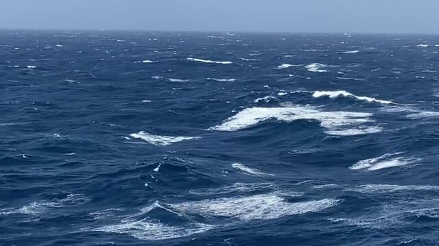 Gray horizon and blue water of the Pacific Ocean. Big waves and turbulent water of the open ocean on a sunny day. View from a cruise ship.
