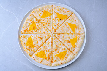 Quesadilla slices on a white plate, each topped with a triangular piece of yellow cheese. Made with flour tortillas and melted cheese inside. Neatly arranged, visually appealing presentation.