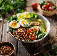 Buckwheat groats with avocado, various vegetables and soft-boiled egg in a ceramic bowl, focus on groats, shallow depth of field. Healthy breakfast suggestion slavic girl diet