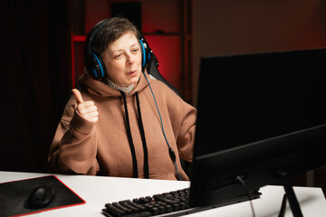 Middle age woman wearing hoodie playing video games using headphones and computer showing gesture...