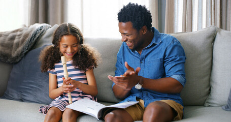 Learning, music and kid with father for flute lesson on sofa with book for notes in home. Education, bonding and dad teaching girl child to play recorder instrument for talent development in house. © peopleimages.com