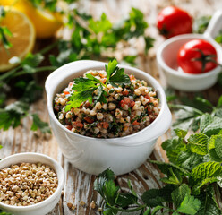 Green buckwheat salad with fresh herbs, tomatoes lemon juice and olive oil in a ceramic bowl, close-up view. Healthy salad suggestion slavic girl diet