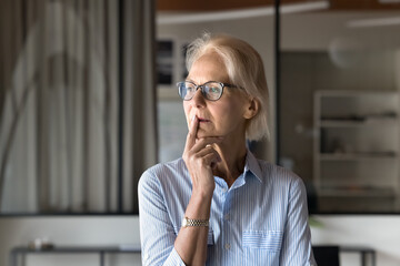 Mature woman with thoughtful expression, looks into distance, deep in thought, contemplate on idea,...