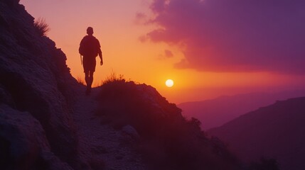 Fototapeta premium A lone hiker silhouetted against a breathtaking sunset walks along a rugged mountainside, embodying solitude and awe.