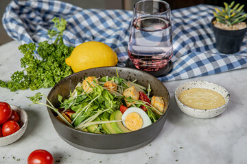 A vibrant salad with fresh vegetables, boiled eggs, and a dressing, accompanied by a glass of water and garnished with lemon, set against a checkered cloth.