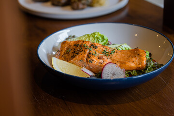 A delicious plate of salmon fillet served with fresh greens, radishes, and a slice of lemon, highlighting a healthy and vibrant meal.