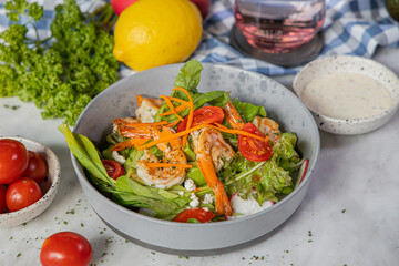 A vibrant salad featuring fresh greens, cherry tomatoes, shredded carrots, and a lemon, served in a bowl, with a glass of pink drink in the background.