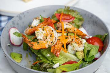 A colorful salad with shrimp, fresh greens, cherry tomatoes, and radishes, drizzled with dressing, served in a gray bowl.