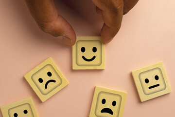 Hand Choosing Wooden Cube with Smile Face Among Sad Faces, Representing Positivity, Decision...