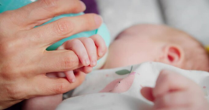 Mom holds newborn baby in her arms, baby drinks adapted formula from bottle held by mother, close-up. Concept of healthy eating, artificial nutrition, infant feeding