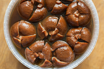 Transparent container holding whole lemons with wrinkled amber skin, immersed in a salty brine,...
