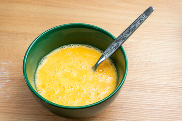 Raw beaten eggs in a ceramic bowl, ready to be cooked into scrambled eggs. Fresh and vibrant yellow with a smooth texture, ideal for breakfast or cooking concepts.