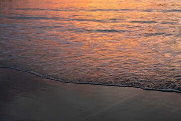 Reddish reflections in the sea on a beach at sunset.
