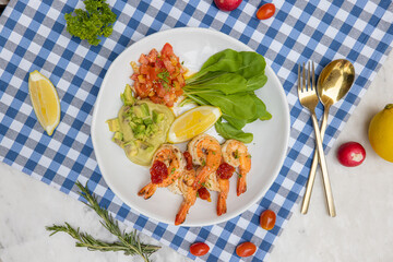 A vibrant plate featuring shrimp, fresh vegetables, and lemon, arranged on a blue-checked tablecloth, showcasing a colorful and appetizing meal.