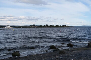 Wellen branden am Strand der Insel Bygdoy in Oslo. Im Hintergrund ist im Oslofjord der Leuchtturm...
