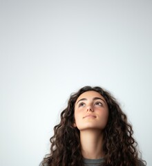 Fototapeta premium Young girl looking up, curly hair, thoughtful expression, neutral background, copy space for text