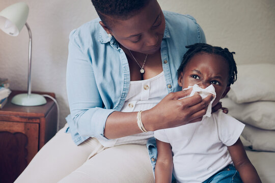 Black family, mom and blowing nose of child in home, support sick kid and help with nasal infection. Mother, daughter and tissue for respiratory disease in bedroom, illness and allergies or hayfever
