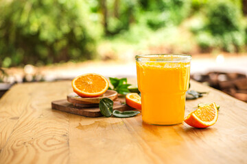 A glass of freshly squeezed orange juice on a wooden table surrounded by orange slices and orange leaves