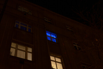 A tall building featuring a bright blue window that is beautifully illuminated during the night time hours