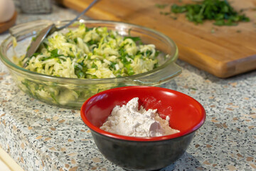 Flour on the background of a glass plate with zucchini pulp grated on a grater and herbs for making pancakes. Close-up