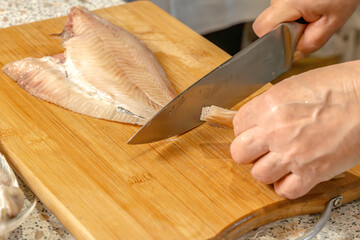 Cook with a knife cuts off the tail of fresh fish. Preparing flounder for frying