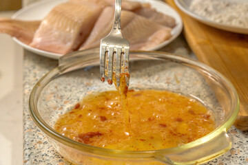 Chef beats raw eggs, salt, red pepper and paprika for liaison with a fork before frying pieces of fresh fish. Close-up