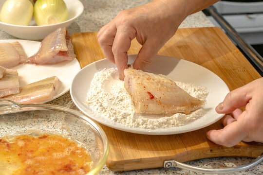 Chef dips pieces of fresh fish in flour before further frying in a frying pan