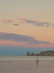 A person walks along the beach with the plane, the sea and the sunset in the background. 